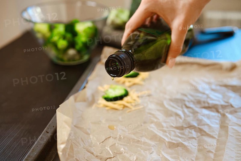 Broccoli florets and cheese are being prepared in a kitchen. Olive oil is drizzled on parchment to enhance flavour. This scene shows the process of making a simple dish at home