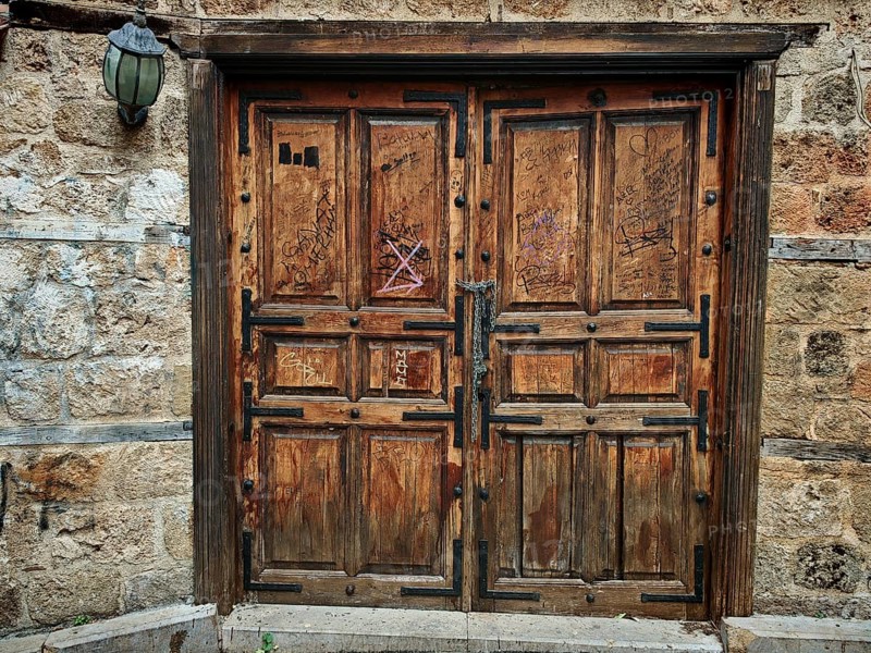 Old wooden door with graffiti on a stone wall, next to it an old lamp, Antalya Turkey
