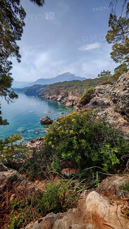 Rocky coastal landscape with clear water, lush vegetation and a Tahtali mountain in the background, Lycian Way, Turkey