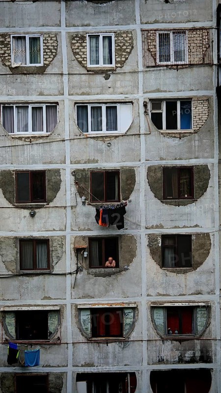 Dilapidated residential building with open windows and people in a simple environment, Tbilisi, Georgia