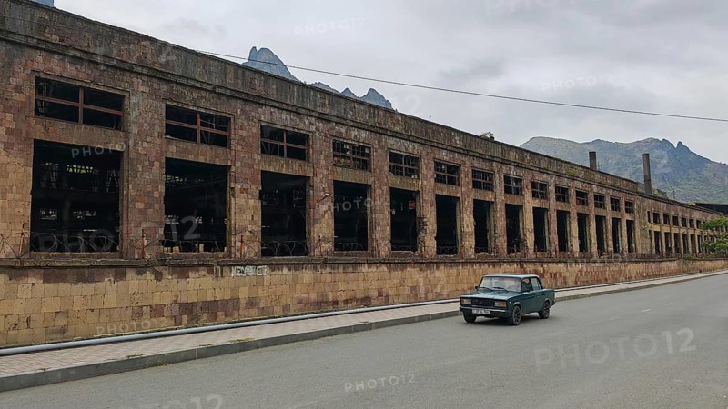 Abandoned large building and a car on a quiet road in the background mountains and clouds, Alaverdi, Armenia