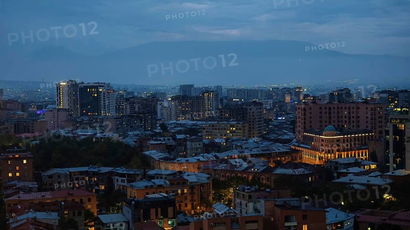 Nighttime city scene at dusk with illuminated buildings and mountains in the background, Yerevan, Armenia