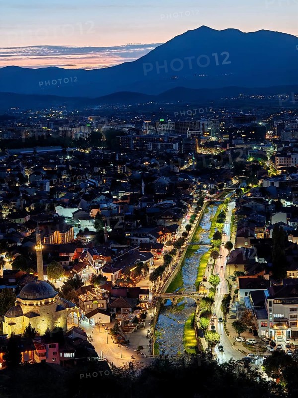 An illuminated urban panorama at night with a central river and mountain backdrop, Prizren, Kosovo