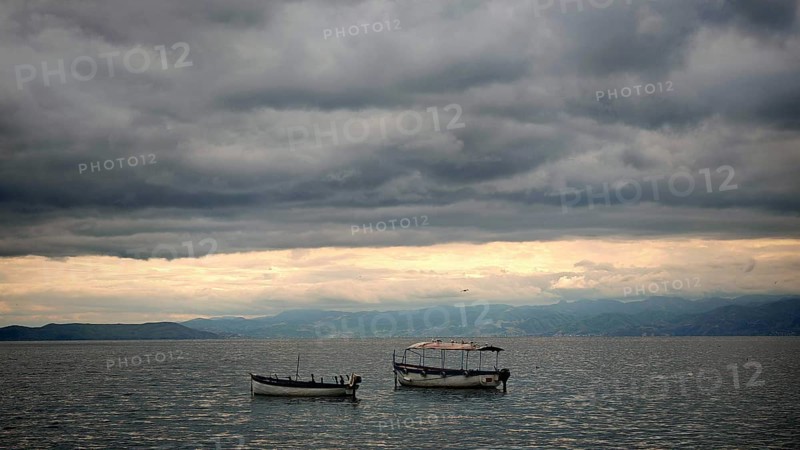 Boats on a still lake under a cloudy sky, peaceful scenery, Orhid Lake, North Macedonia