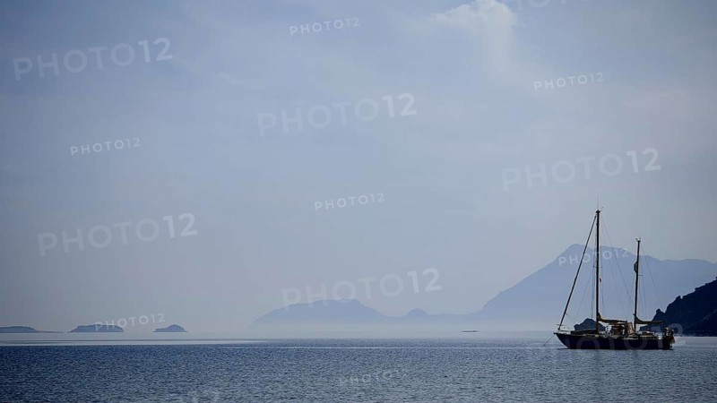 A sailboat in a foggy atmosphere on the sea with silhouetted mountains, Antalya, Turkey