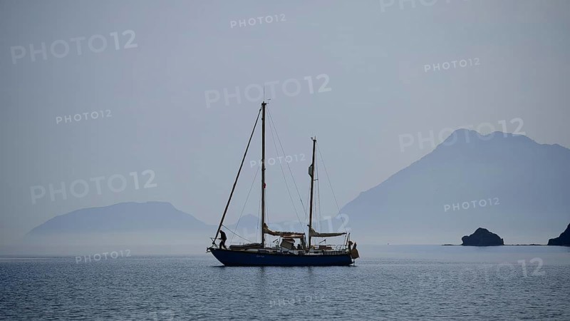 A lonely sailboat in the still sea with misty mountains in the background, Antalya, Turkey
