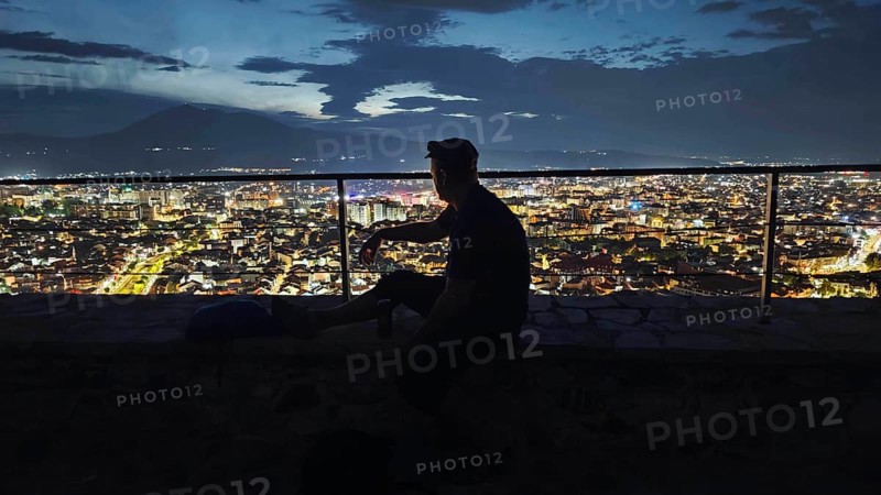 Person in front of illuminated cityscape at night, relaxed atmosphere, Prizren, Kosovo