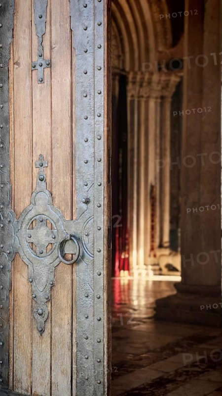 A massive wooden door with detailed metal ornaments opens to a Gothic interior, Kosovo