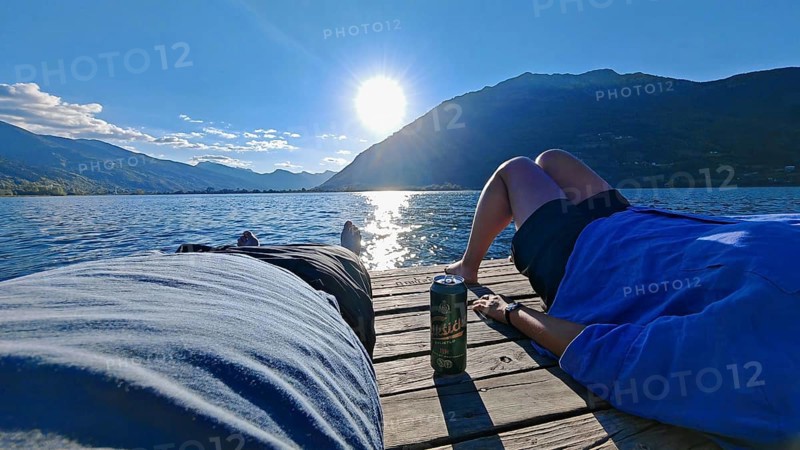Two people relax on a jetty in front of an impressive mountain backdrop at the lake, Plav Lake, Montenegro