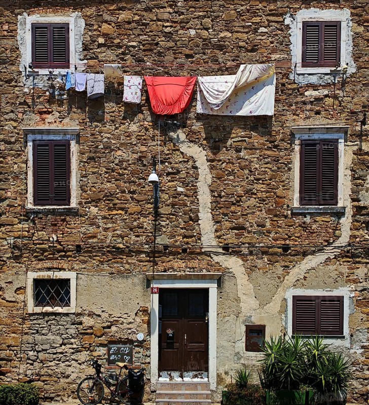 Rustic stone wall with hanging clothes and closed shutters, Koper, Slovenia