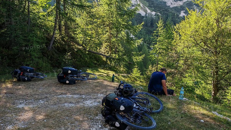 Person having a picnic in the woods with bicycles in a meadow surrounded by mountains