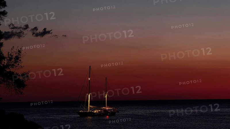 Sailing boat on still sea at sunset, illuminated by dwindling daylight