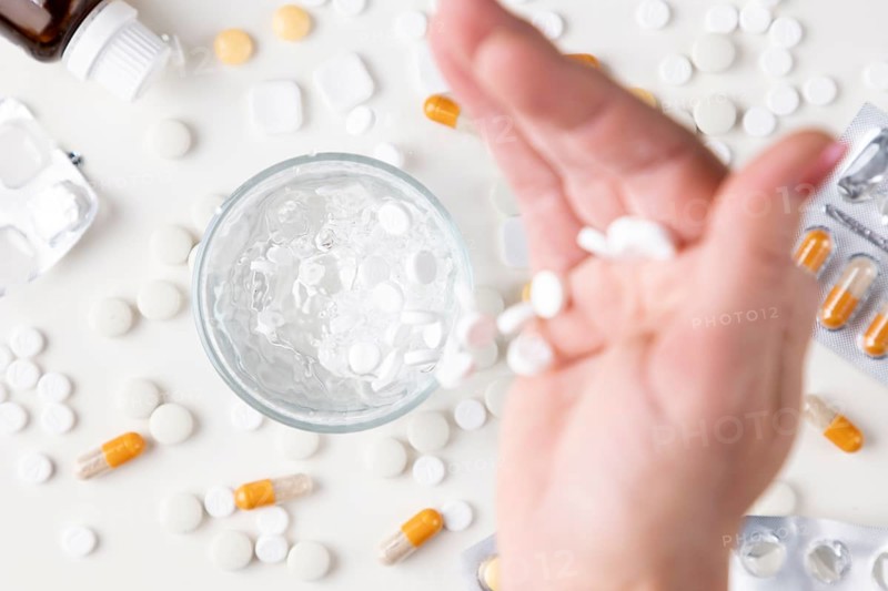 Hand pouring white tablets into a glass with water on a light background