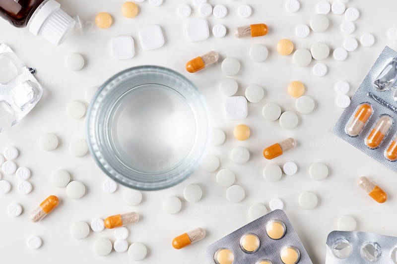 Table with scattered tablets, blister packs and a glass of water