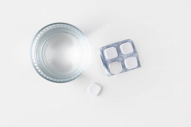 Glass of water with packaging and tablets on a white surface