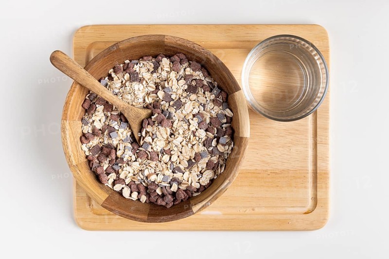 Rustic bowl with cereal and wooden spoon on a wooden board, water glass next door