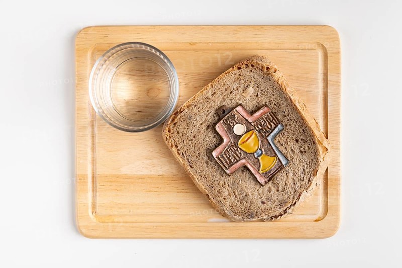 Bread with cross symbol on a wooden board with a glass of water next to it, white background