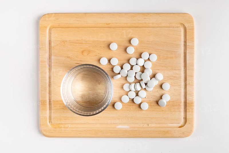 Wooden board with glass of water and scattered tablets