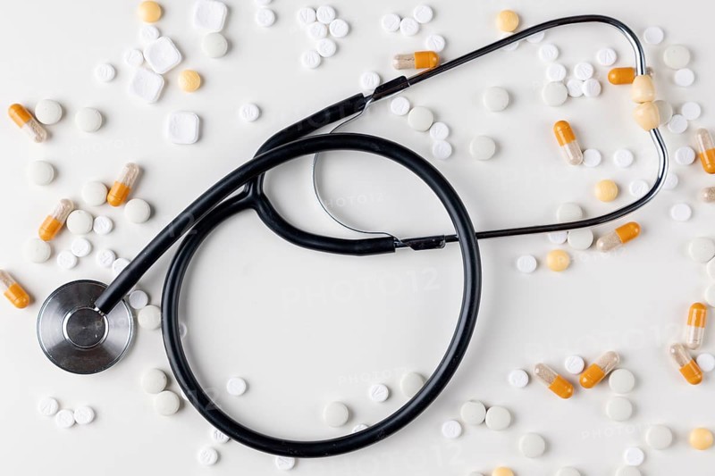 Stethoscope lies on a white surface surrounded by tablets and capsules