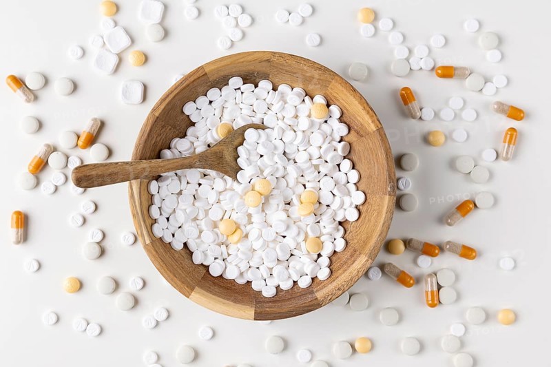 Wooden bowl filled and surrounded by tablets and capsules on light background