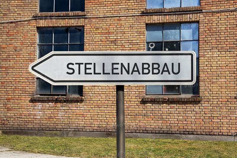(photo montage) Directional arrows with the inscription JOB REDUCTION in front of an old industrial building