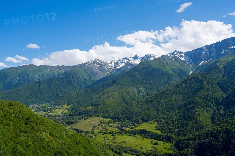 Green valley with densely wooded slopes and distant mountains under blue sky with clouds, landscape near Iskari, Mingrelia and Upper Svaneti, Samegrelo-Zemo Svaneti, Svaneti, High or Greater Caucasus, Georgia