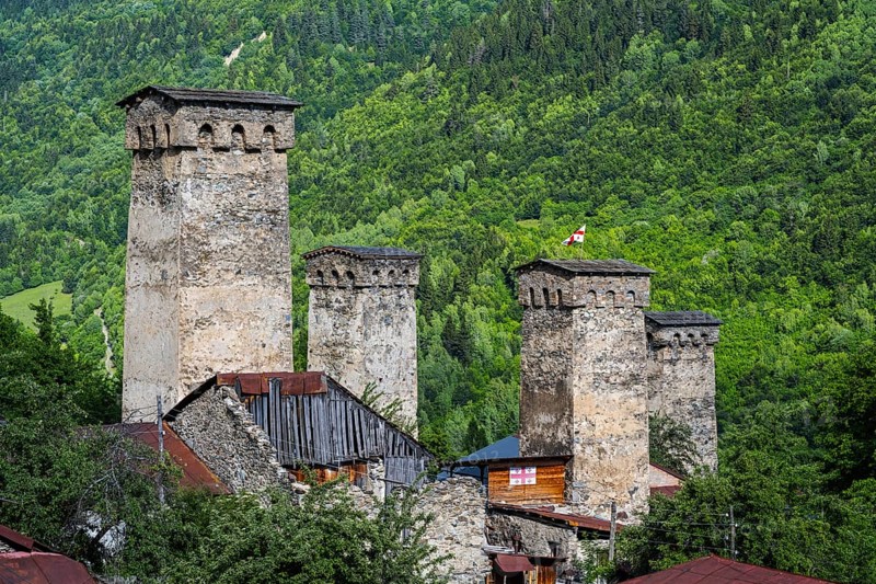 Historic defense towers surrounded by green trees and forest, in the background a small flag, defences in Soli, Mestia, Mingrelia and Upper Svaneti, Svaneti, Caucasus, Georgia