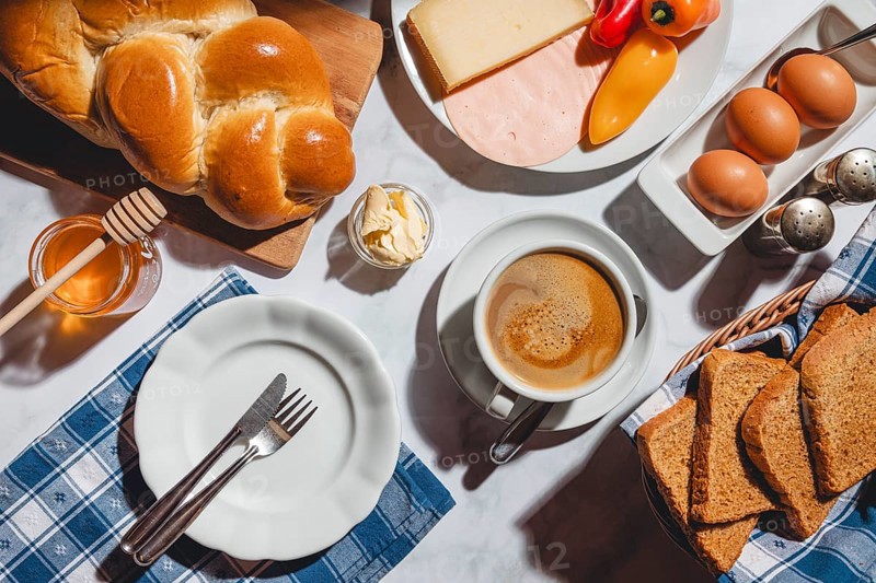 Breakfast with toast, stollen, honey, cheese, ham, coffee, butter, peppers and eggs on a table