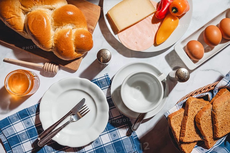 Breakfast with toast, stollen, honey, cheese, ham, peppers and eggs on a table