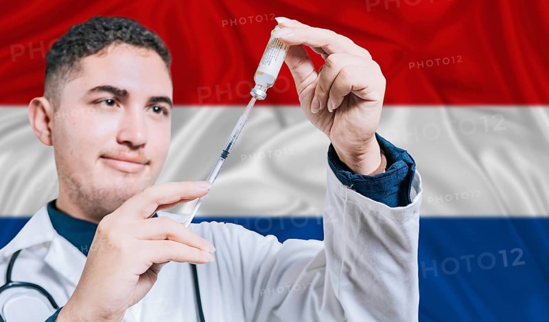 Doctor holding syringe on Netherlands flag background. Medical professional holding syringe with Dutch flag in the background