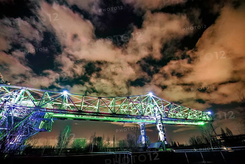 Illuminated bridge at night under a dramatically cloudy sky with green light, Landschaftspark Duisburg Nord, Duisburg, North Rhine-Westphalia, Germany