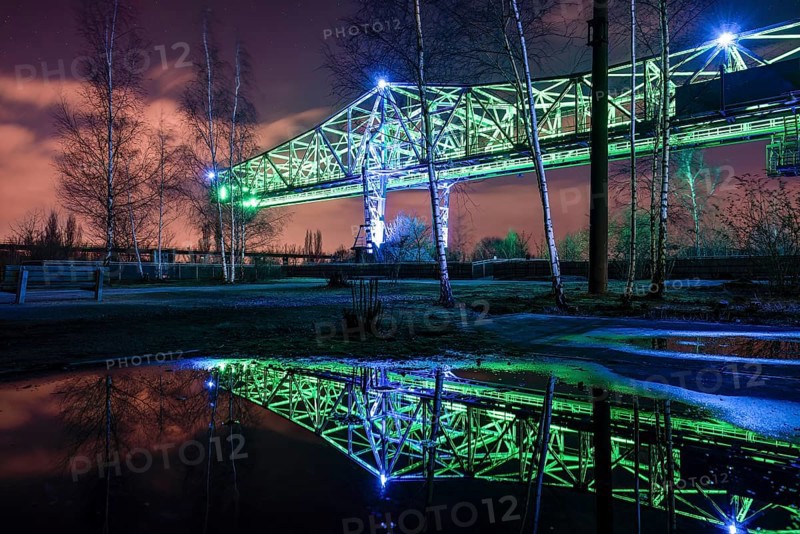 Green-lit bridge structure at night reflecting in a water surface, Landschaftspark Duisburg Nord, Duisburg, North Rhine-Westphalia, Germany