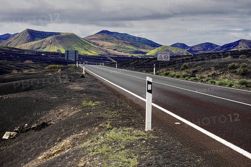 Empty road leads through a volcanic mountain landscape under cloudy sky, Yaiza Lanzarote