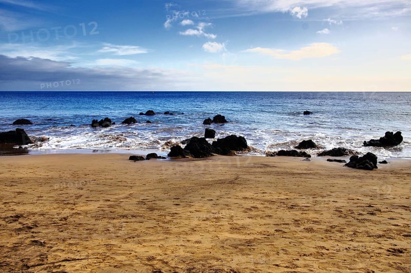 Peaceful sandy beach with rocks and calm sea under a wide sky, Puerto del Carmen Lanzarote