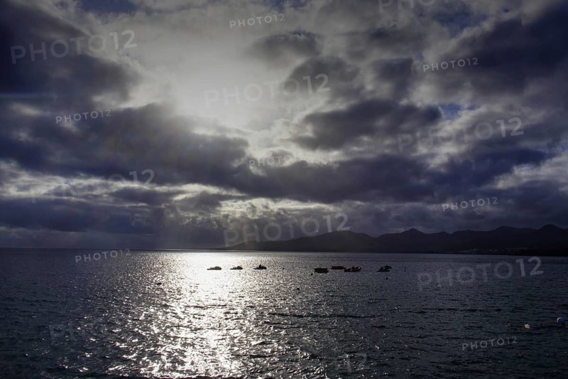 Dramatic atmosphere over the sea, clouds obscuring the sun, reflecting light on the water, Puerto del Carmen Lanzarote