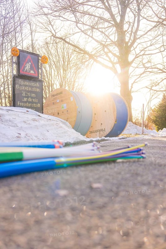 Colored cables in front of cable rolls in sunlight along a snowy road, fiberglass groundbreaking, Freudenstadt, Germany