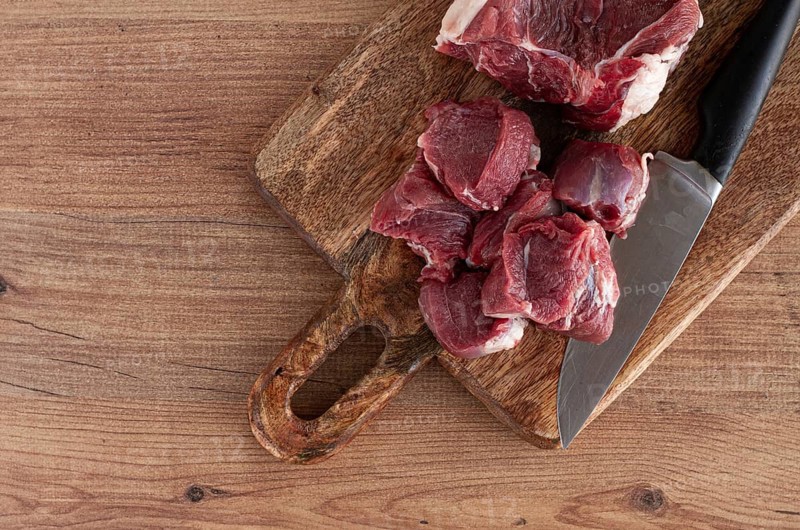 Raw beef meat, sliced on a cutting board, with a knife, no spices, no herbs, top view, wooden table, homemade, no people