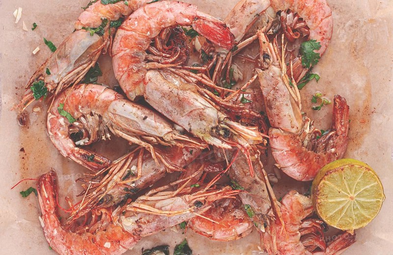 Juicy grilled shrimp, placed on a baking sheet lined with parchment paper, garnished with herbs and lemon