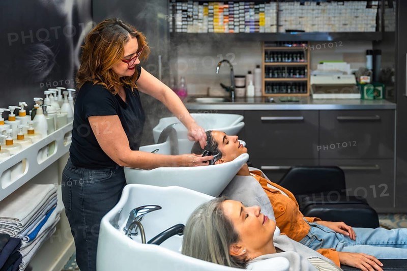 Professional hairdresser gently washing a young woman's hair at a salon basin, providing relaxing shampoo, conditioner and pampering hair care for client wellbeing and comfort