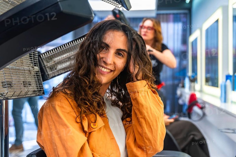 Woman with curly hair smiling while receiving hair drying and treatment at a modern hair salon, feeling beautiful and relaxed during her beauty routine