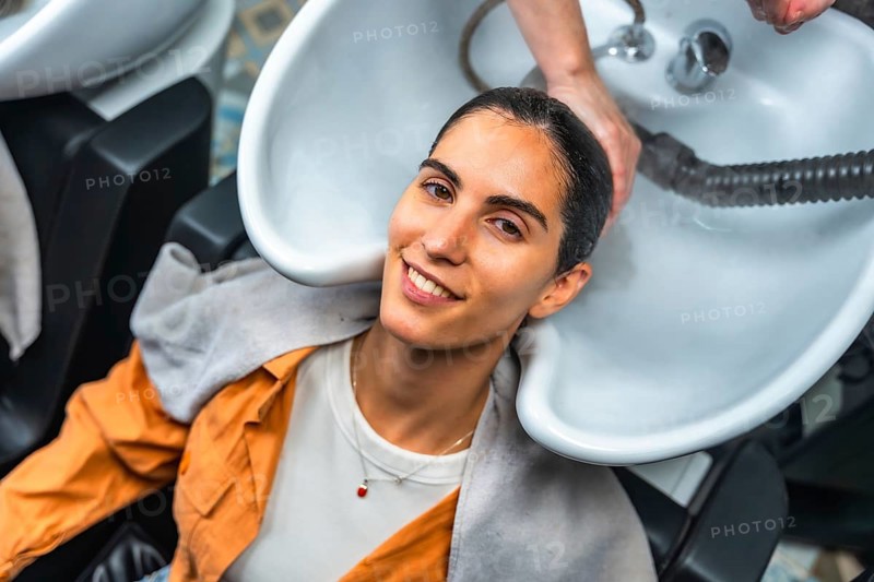 Young woman smiling and relaxing as a hairdresser shampoos and rinses her hair at a professional salon sink, enjoying pampering, scalp massage and beauty care