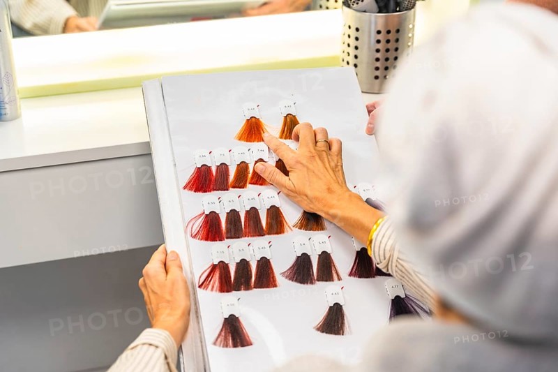 Client selecting desired hair dye shade from a detailed color chart while sitting in a hair salon, making a beauty decision for a new look or hair treatment