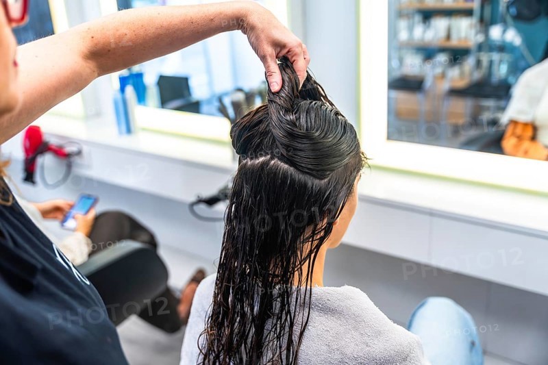 Hairdresser holding sections of wet hair on a woman's head in a bright salon, preparing for a haircut or styling session, focusing on professional beauty treatment