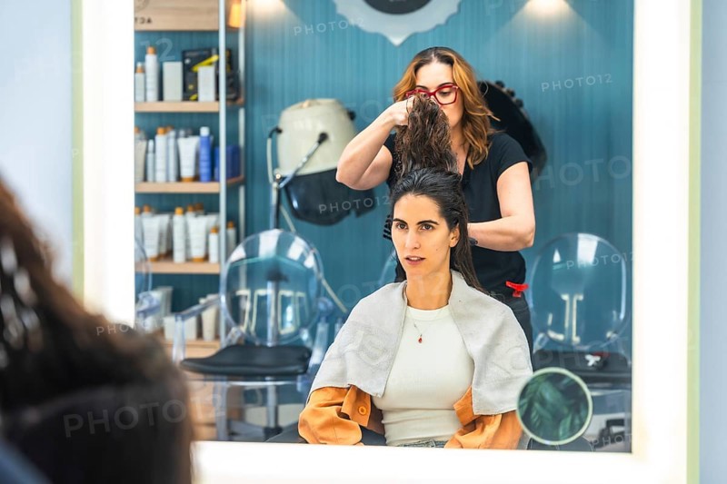 Hair stylist preparing a customer's wet hair for a cut and styling, with the woman looking forward in the modern hair salon setting reflected in a mirror