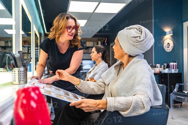 Hairdresser and female client discussing hair color and style options using a color chart, representing consultation, beauty, and professional service in a modern salon environment