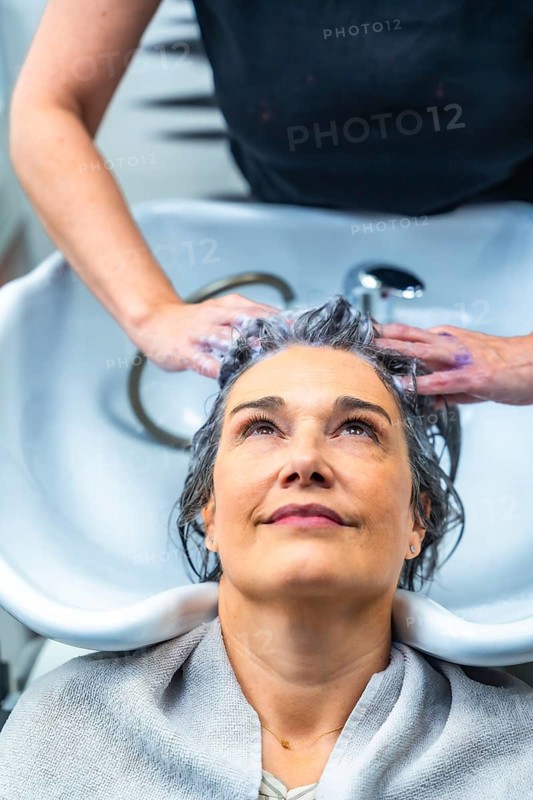 Woman with gray hair receiving a shampoo and head massage from a hairstylist at a modern hair salon, experiencing professional care and relaxation during a beauty treatment