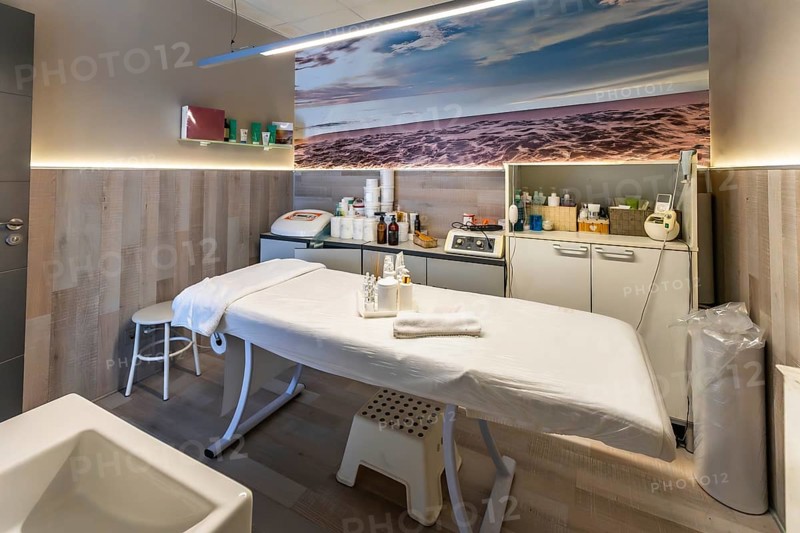 Beauty salon treatment room offering services for skin care, massage, and wellness, featuring a comfortable bed, professional equipment, and a calming ocean themed wall art