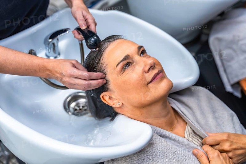 Senior woman smiling as a professional hairdresser washes and massages her hair at a salon sink, enjoying a relaxing shampoo treatment and pampering salon experience