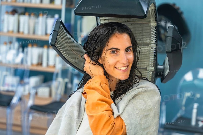 Woman relaxes under a salon hair dryer during a pampering hair treatment, smiling with wet hair as she enjoys beauty, self care and professional styling for a fresh look