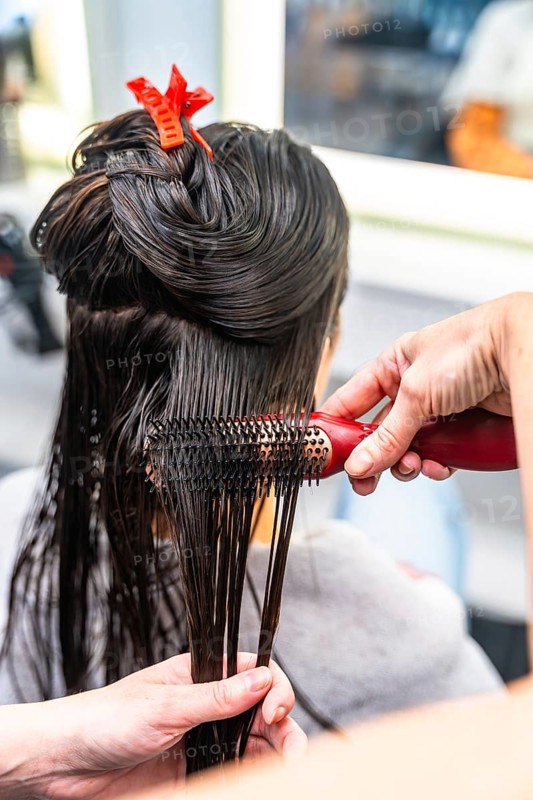 Hairdresser performing a hair styling service on a female client, brushing her wet dark hair after washing and preparing it for further treatment in a beauty salon